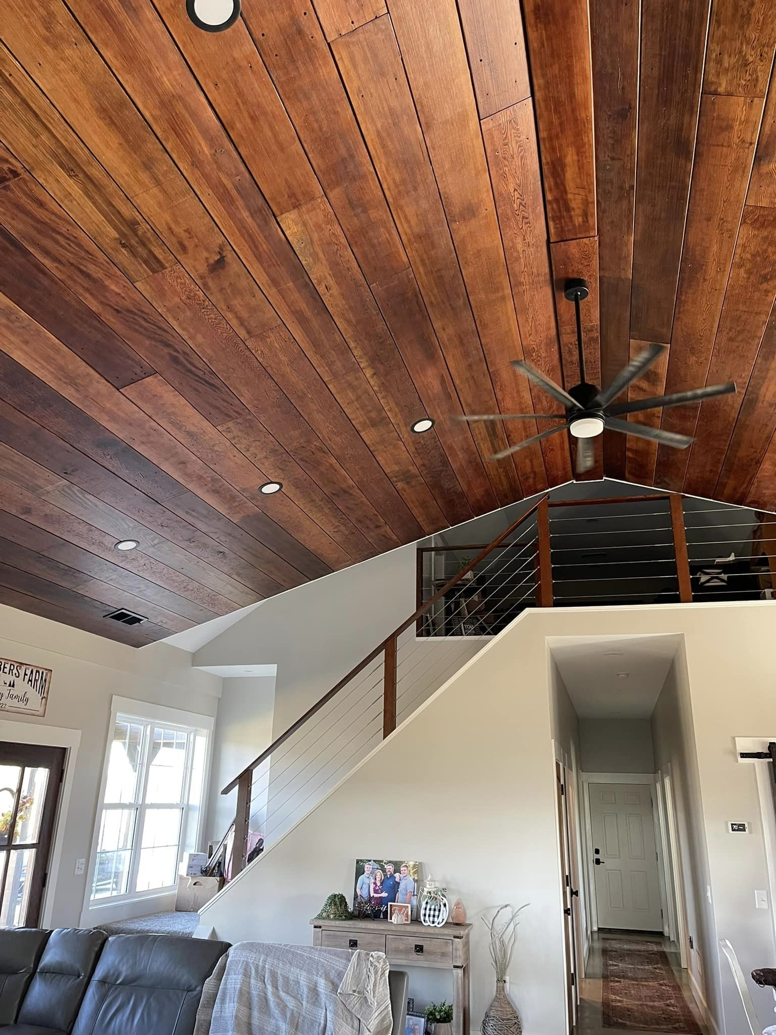 A living room with a wood-plank ceiling and a loft area. A staircase leads to the loft, and a ceiling fan is visible.