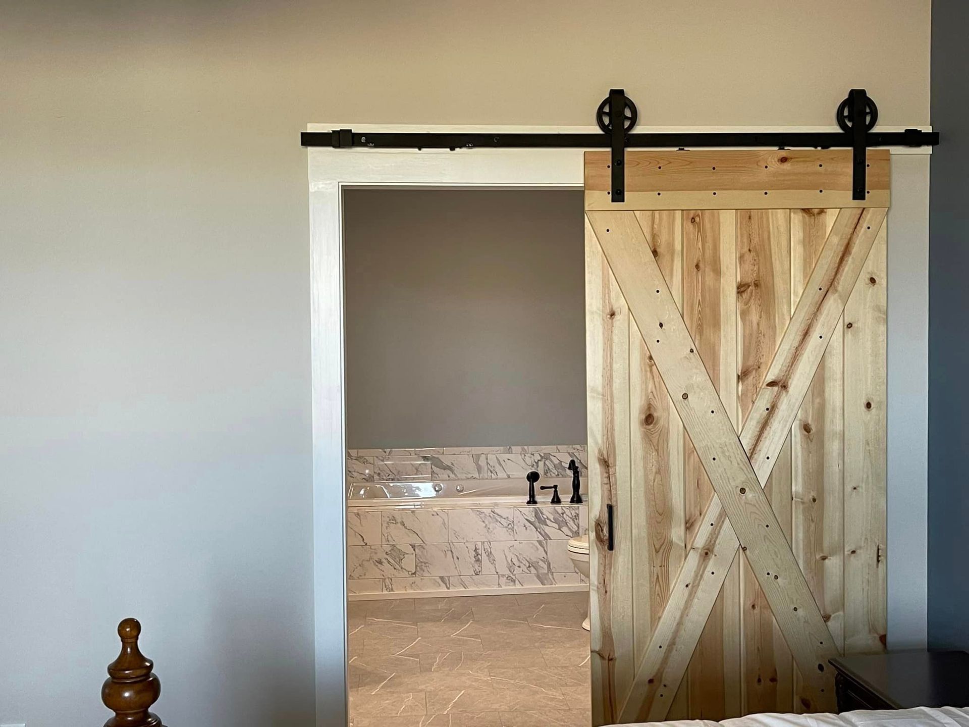 Barn door partially open to reveal a bathroom with a bathtub. The door is wooden and rustic, with black hardware.