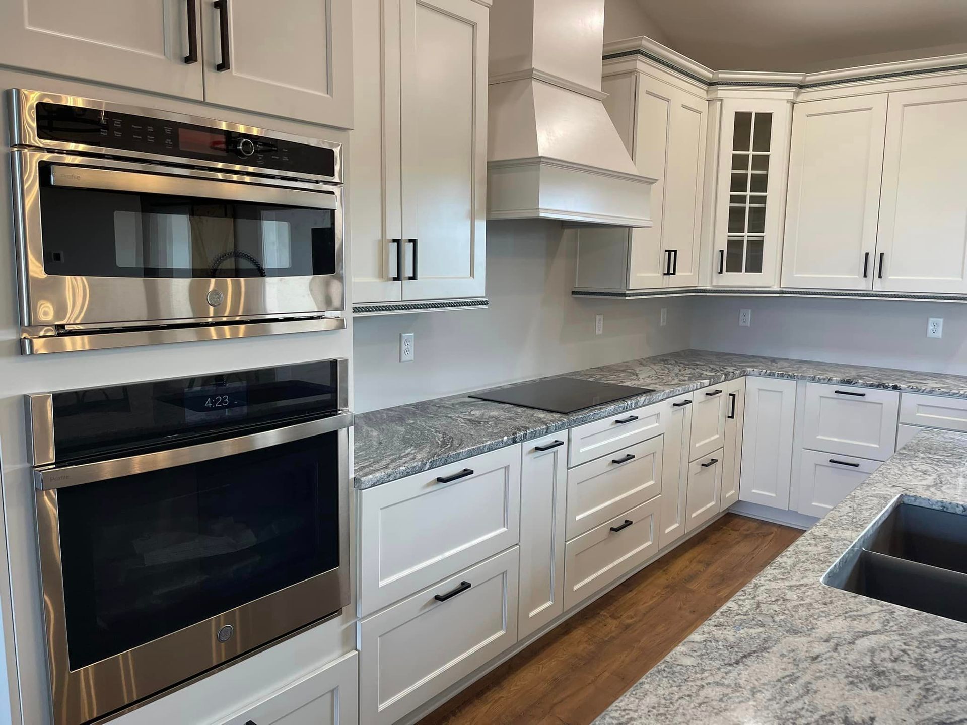 White kitchen with granite countertops and stainless steel appliances, including an oven and microwave.