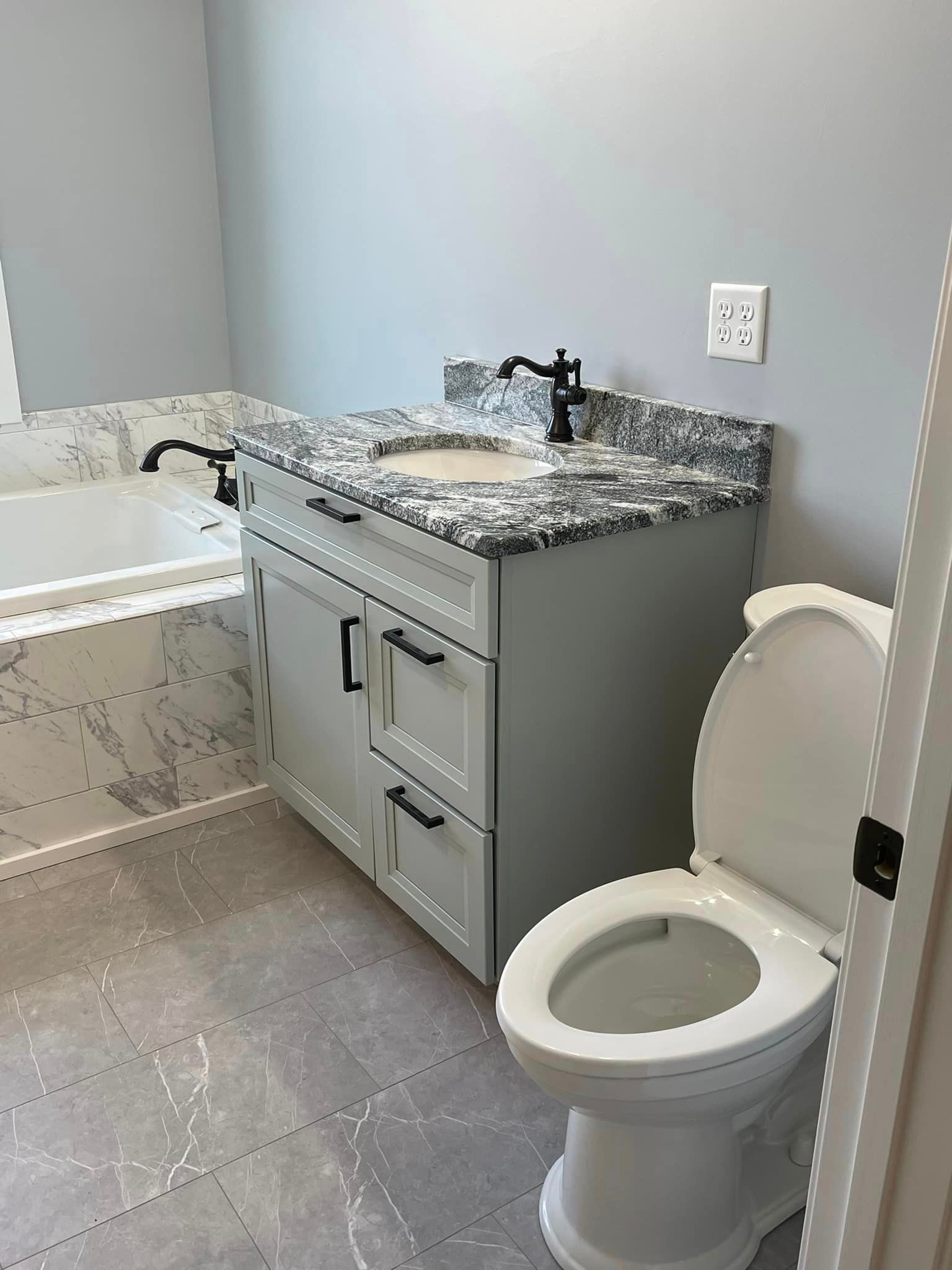 A gray bathroom features a vanity with black fixtures, a toilet, and a bathtub partially visible.