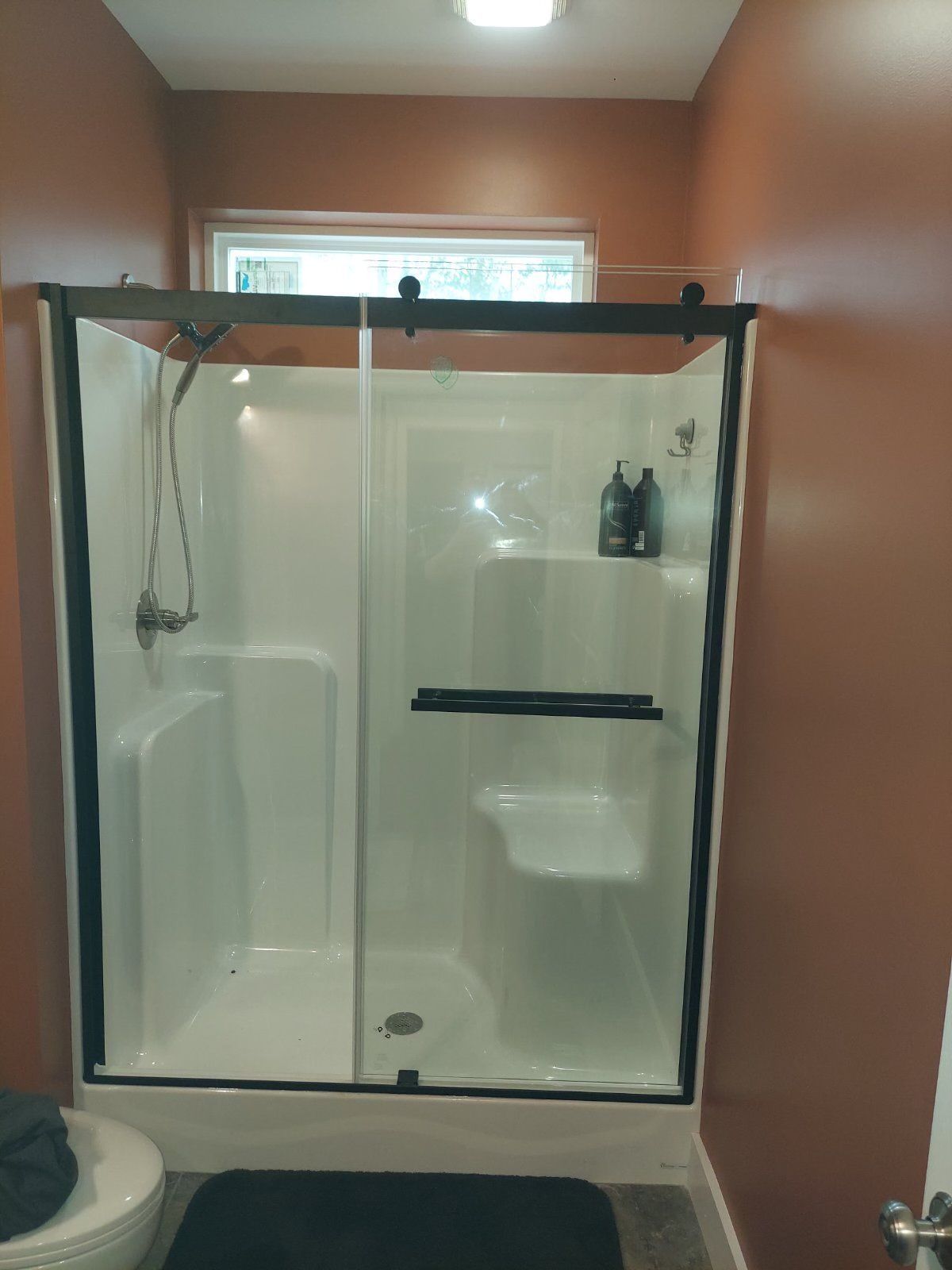 A small bathroom features a white shower with black trim and sliding glass doors, set against orange walls.