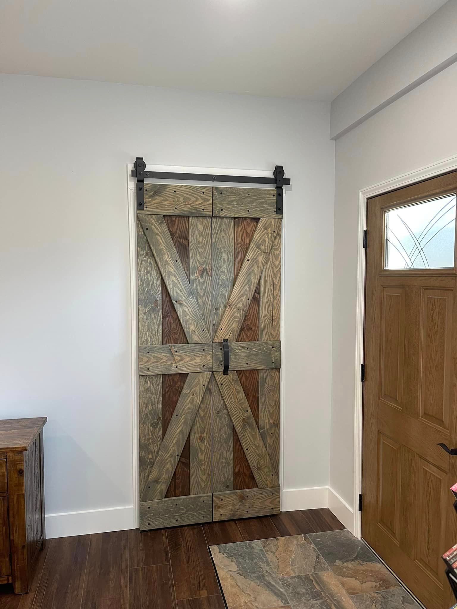 Barn-style sliding door made of weathered wood, with a dark metal track. A wooden door is on the right.