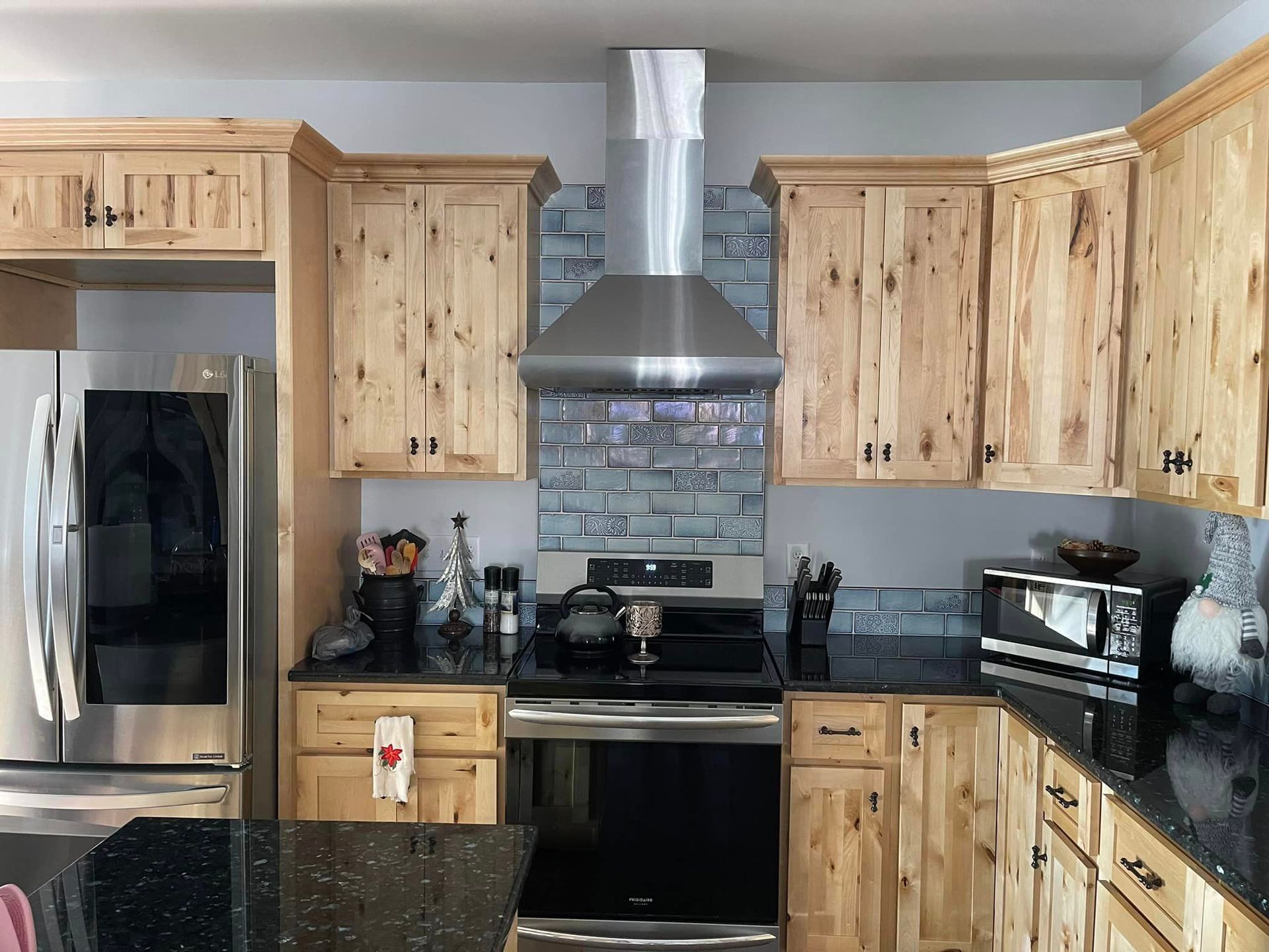 Kitchen with light wood cabinets, black countertops, and stainless steel appliances. Blue-gray backsplash.