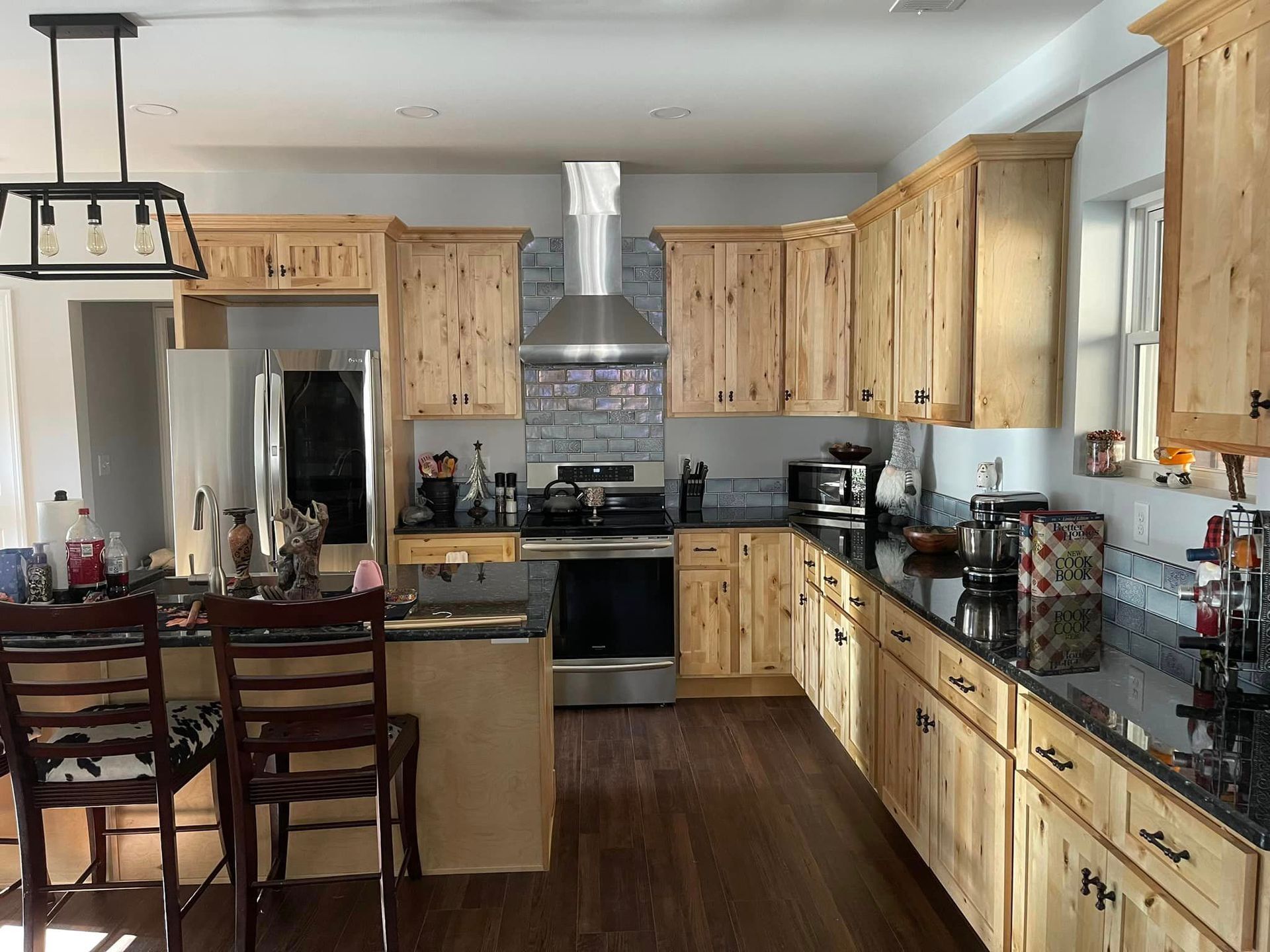 Kitchen with light wood cabinets, stainless steel appliances, dark countertops, and a breakfast bar with stools.