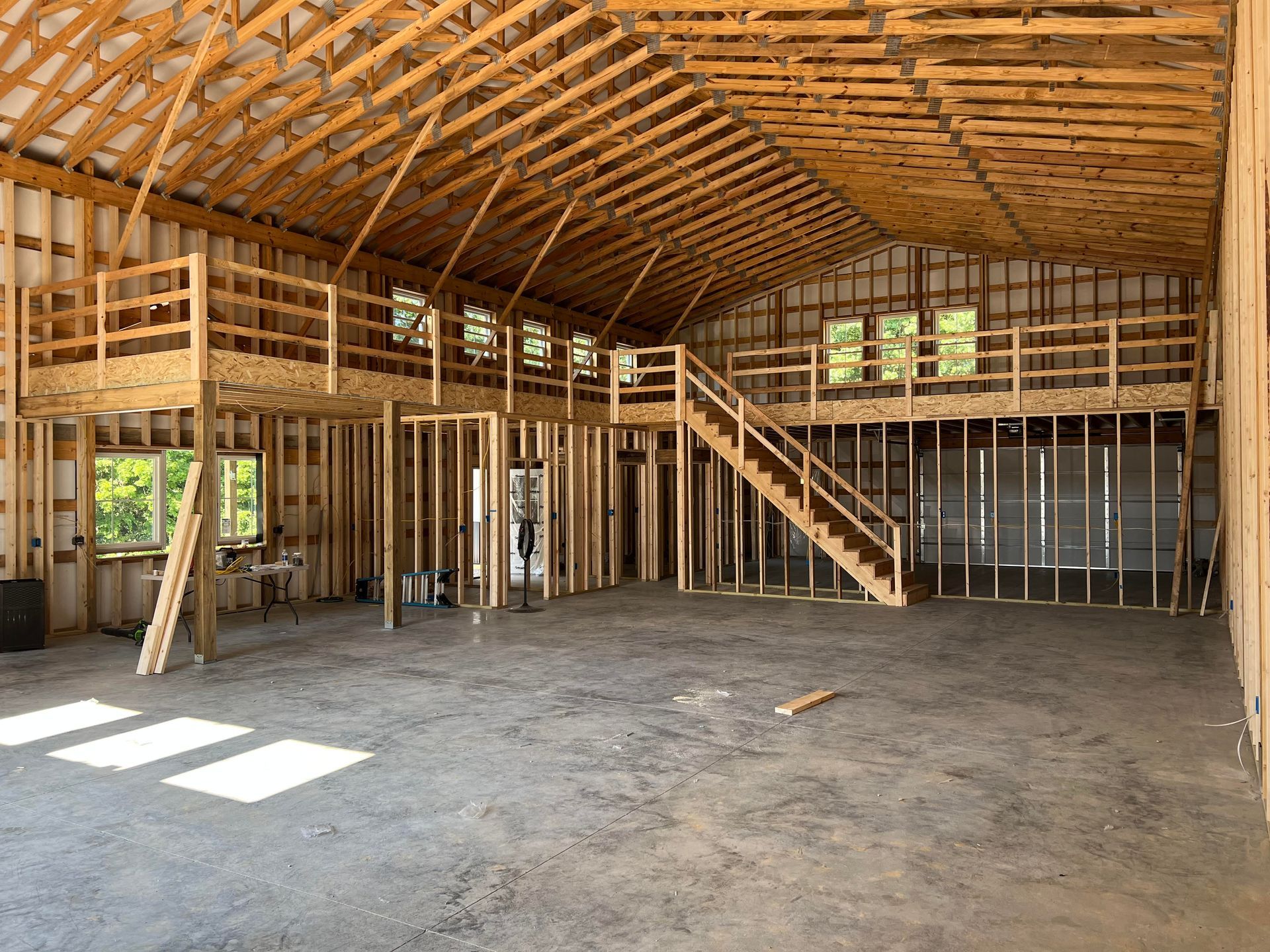 Interior view of a large wooden building under construction. A concrete floor, unfinished walls, and a second-story mezzanine are visible.