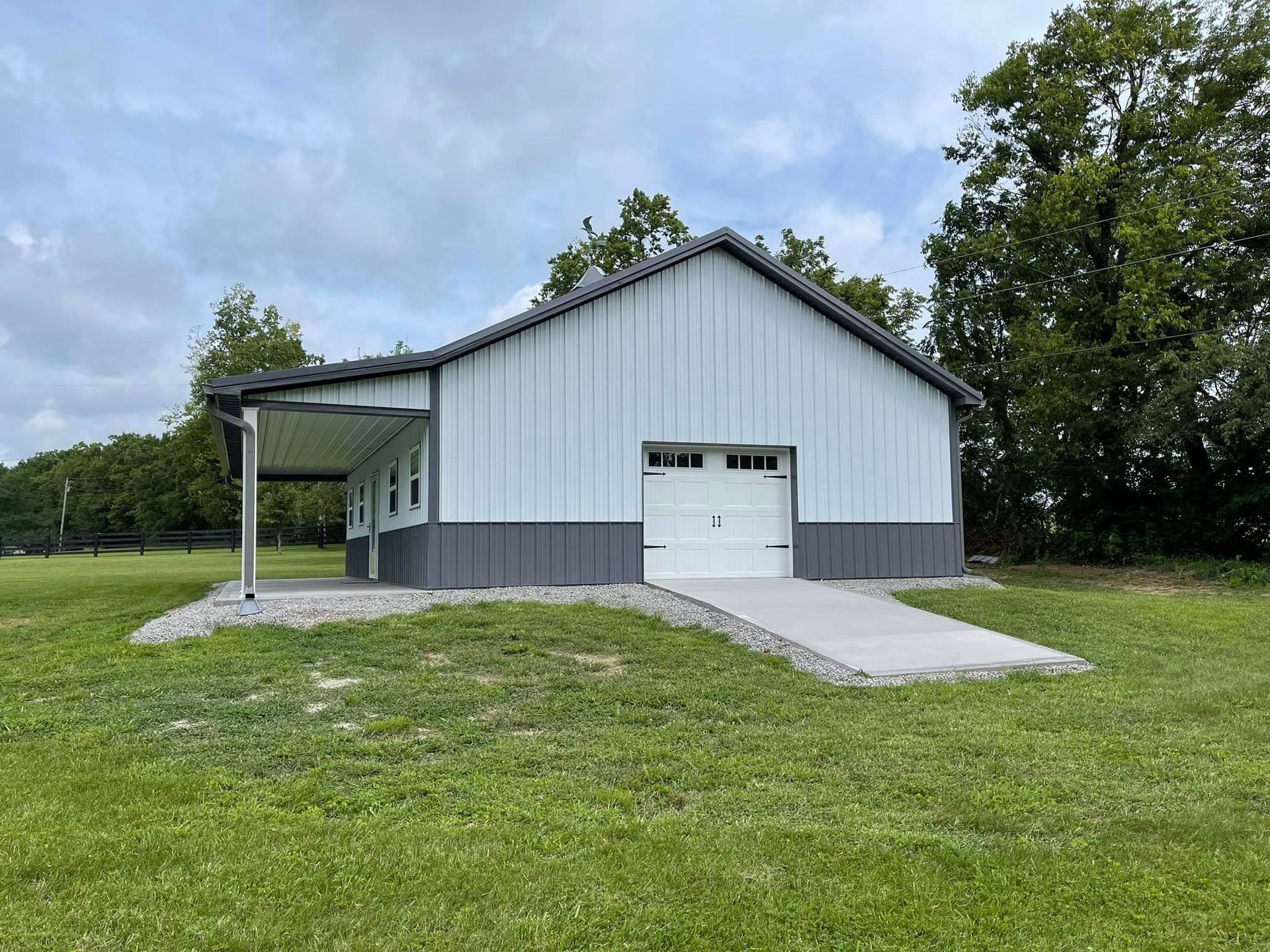 A light blue and gray metal garage with a concrete ramp and a covered carport, set in a grassy yard.