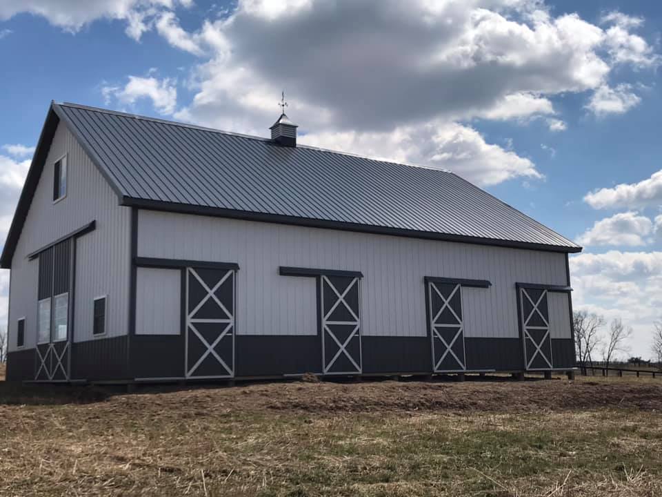 White and gray barn with sliding doors on a grassy field under a cloudy sky.