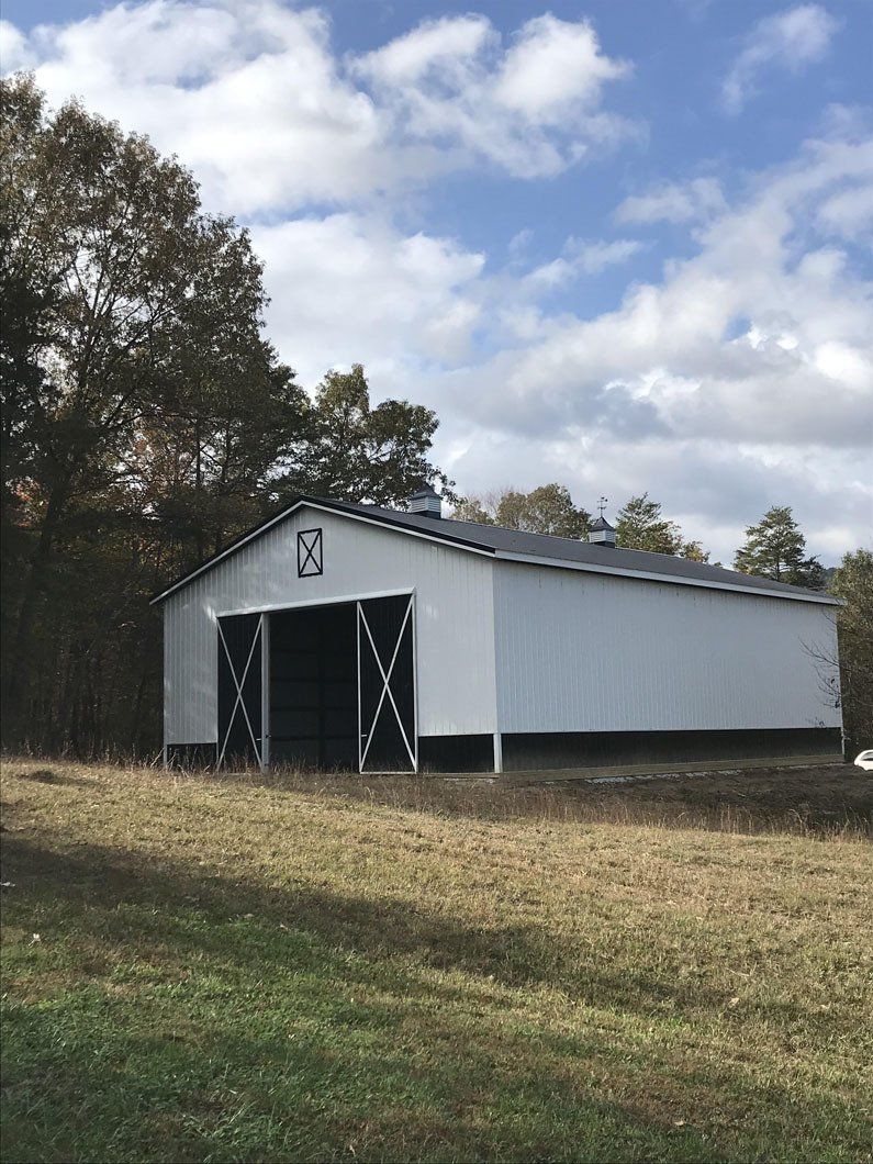 White metal barn with black trim, open doors, on a grassy field under a cloudy sky.