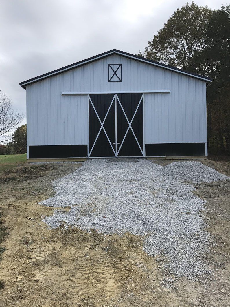 Light blue barn with black trim and a gravel driveway.
