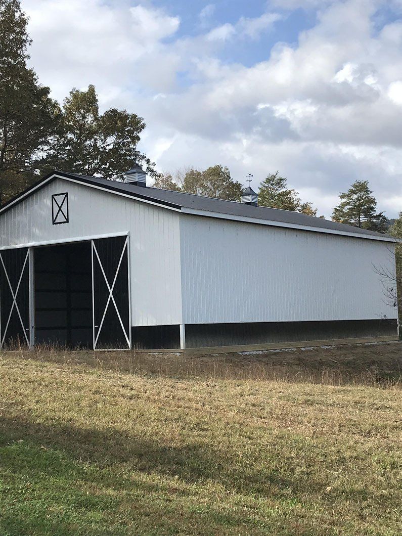 White barn with a black roof and large sliding doors, set in a grassy field under a cloudy sky.