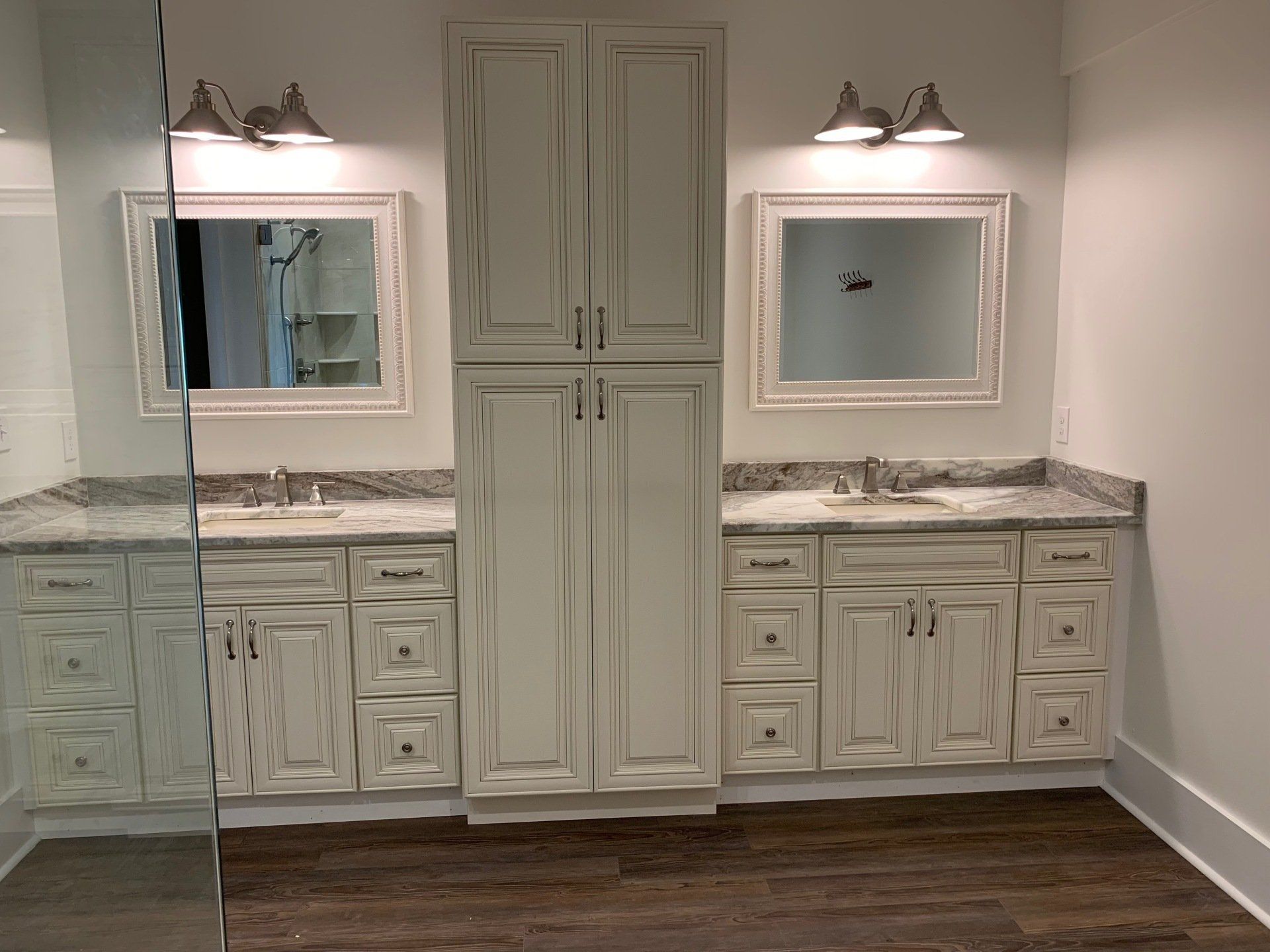 Bathroom with two vanities, a tall cabinet, and mirrors, all in white with gray countertops, on a dark wood floor.