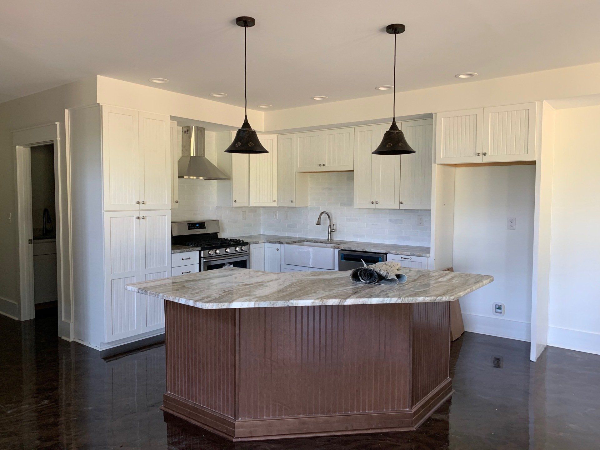 Kitchen with white cabinets, brown island with granite countertop, and two black pendant lights. Dark wood floors and light walls.