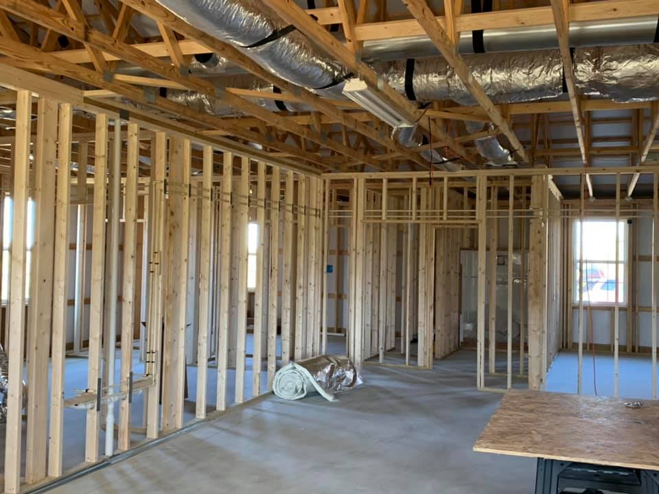 Interior of a building under construction with wooden framing. Stud walls are visible, with a concrete floor and exposed ceiling.