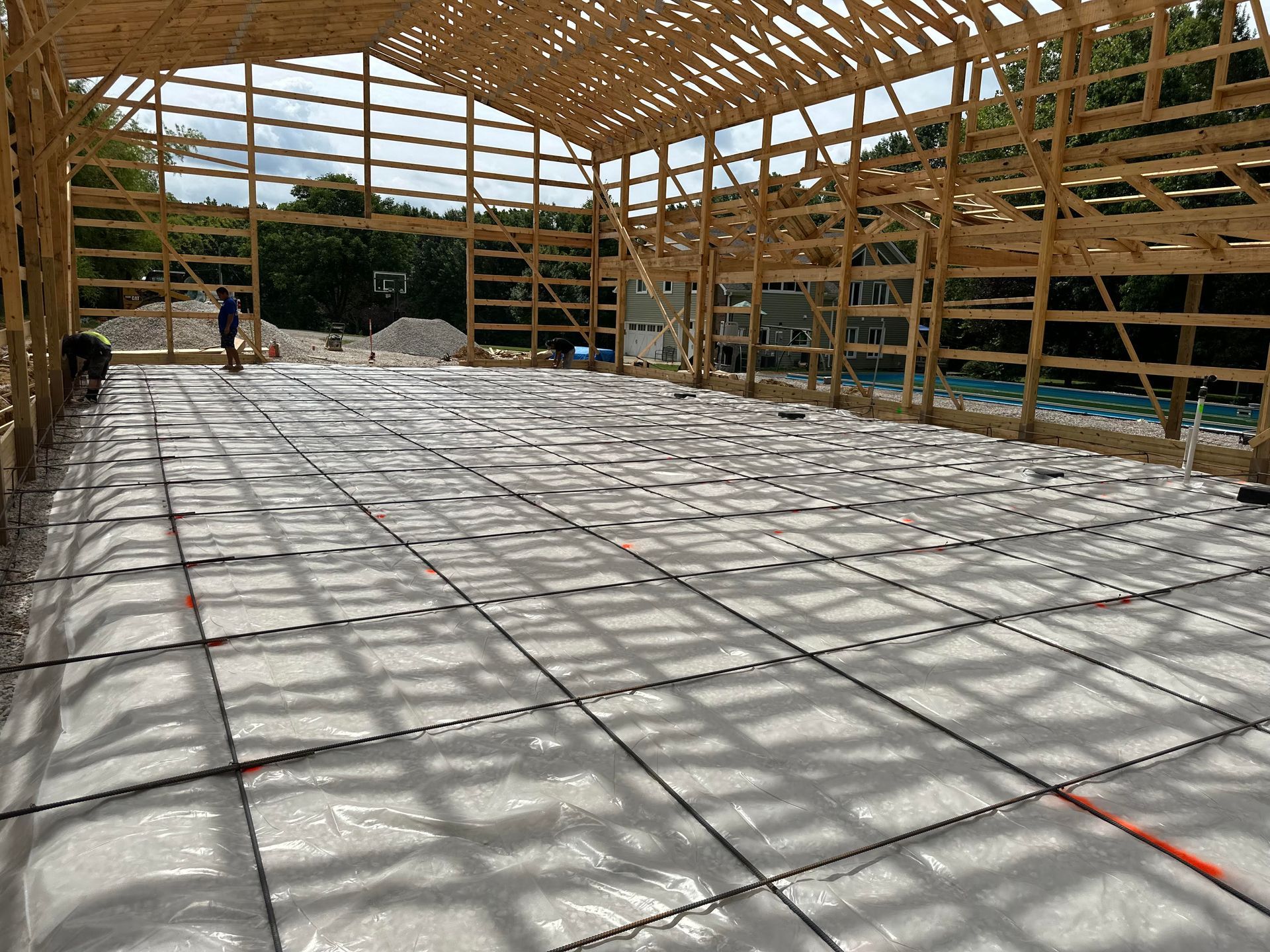 Construction site: Wooden frame of a large building with a grid of black pipes laid on a plastic sheet over the floor.
