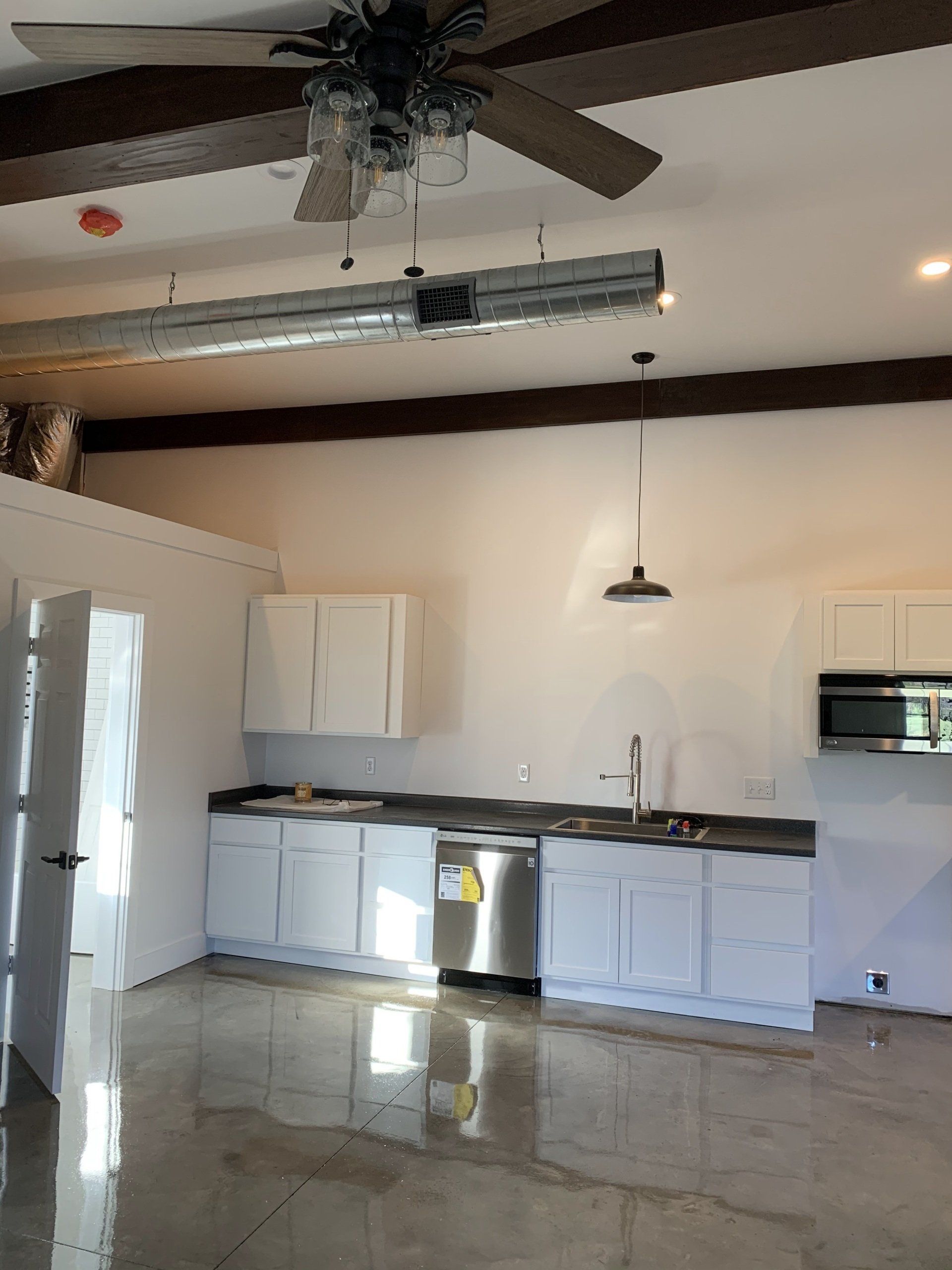 A bright, unfinished kitchen with white cabinets, stainless steel appliances, and exposed ceiling beams.