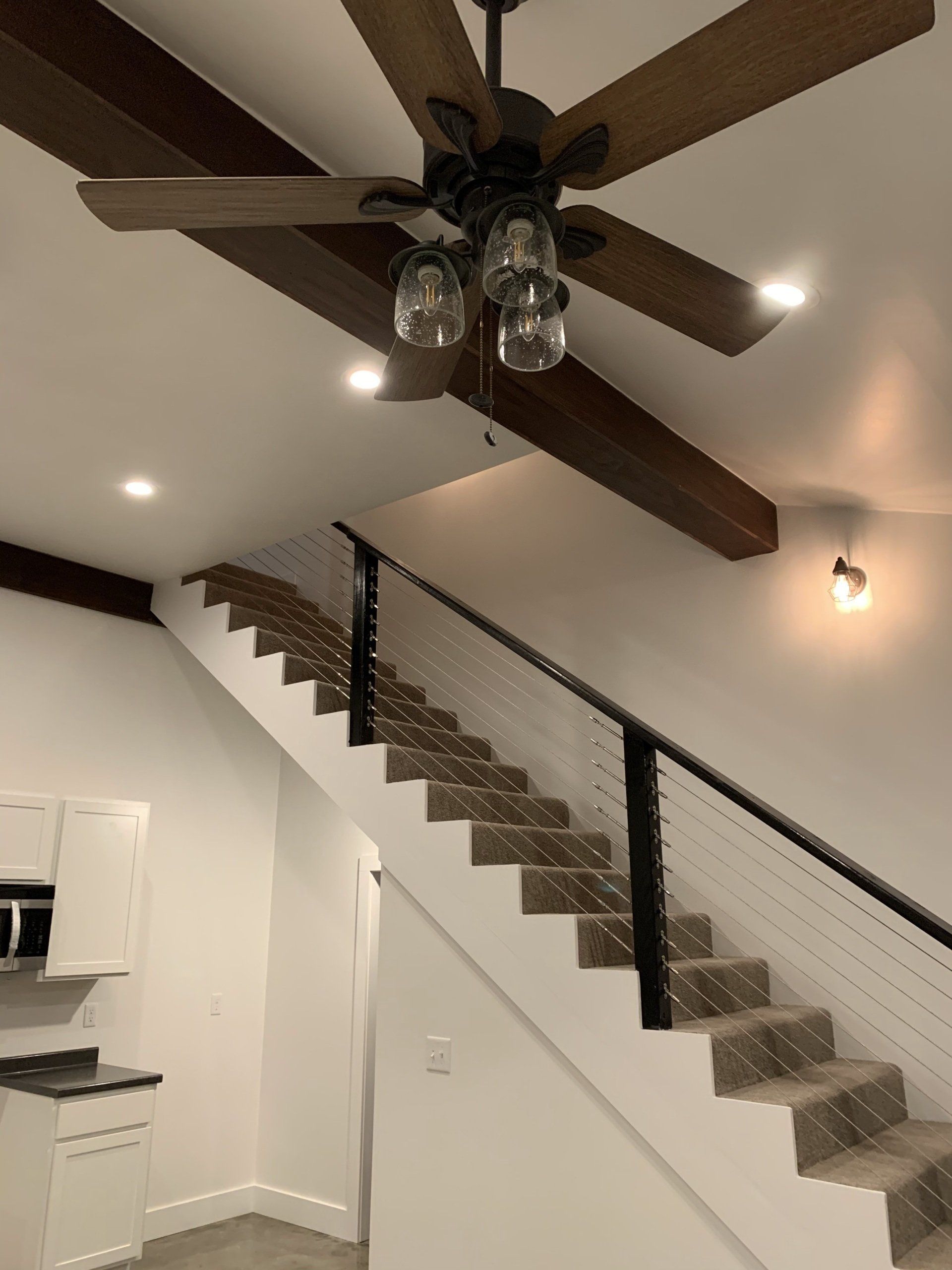 Staircase leading up with black handrails, carpeted steps, and overhead ceiling fan in a modern white interior.