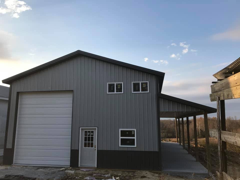 A two-story gray metal building with a large garage door, windows, and a covered walkway.  A door is also present on the first floor.
