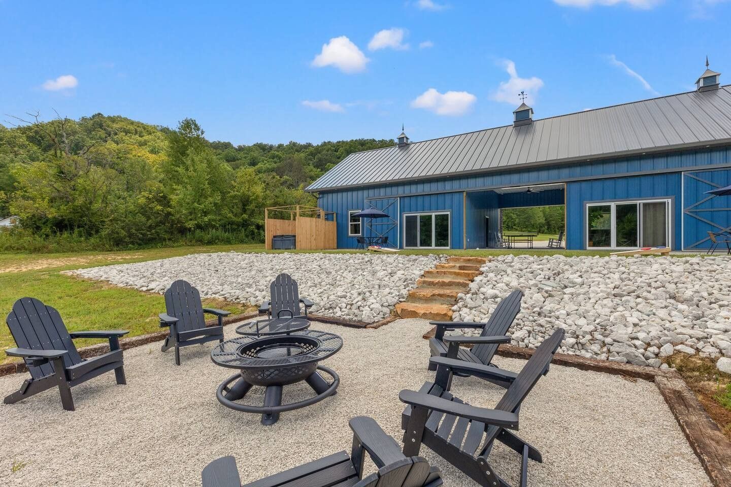 Blue barn with an outdoor seating area, fire pit, and Adirondack chairs on a gravel patio.