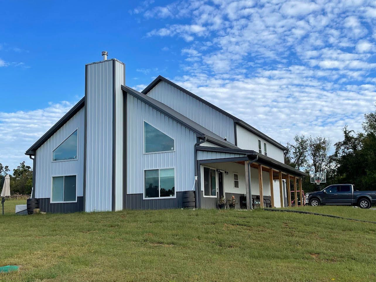 A large, modern barn-style building with a metal exterior stands on a grassy field under a partly cloudy sky.