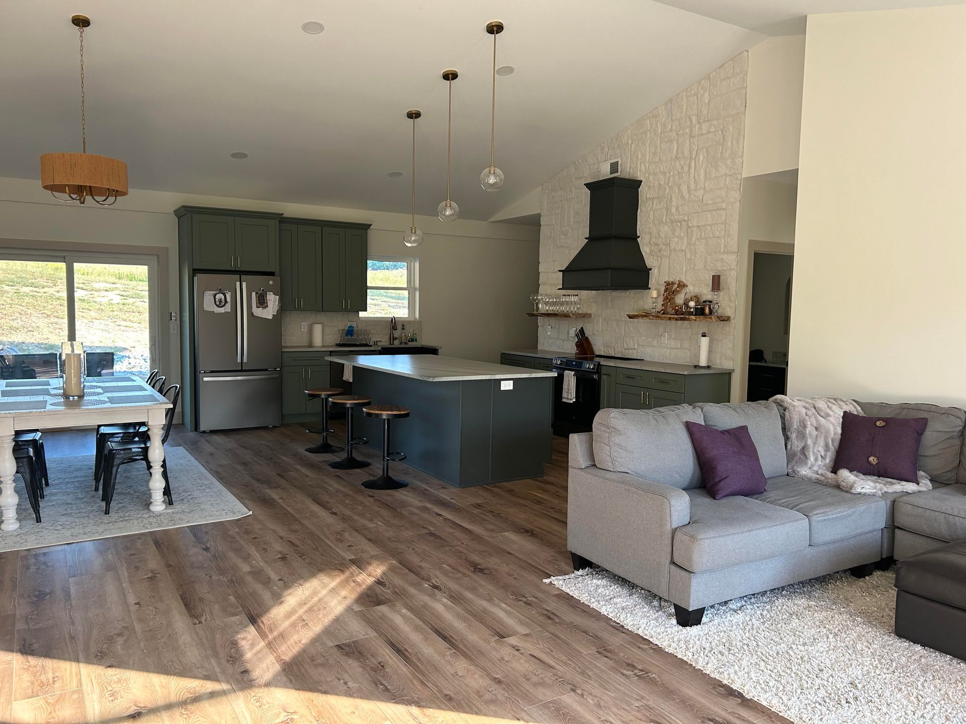 Open-concept kitchen and living room with grey cabinets, dark green island, and a grey sectional sofa.
