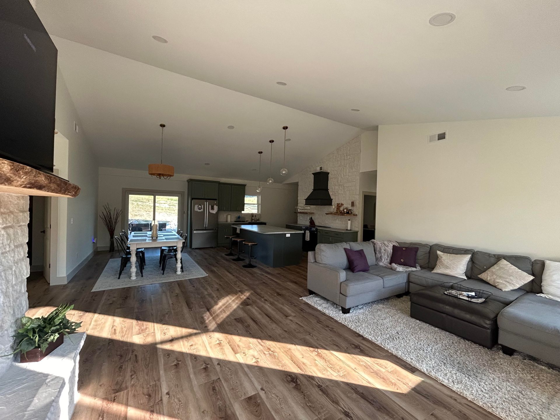 Open-concept living space with a kitchen, dining area, and living room. Hardwood floors, a gray sectional sofa, and a dining table are visible.