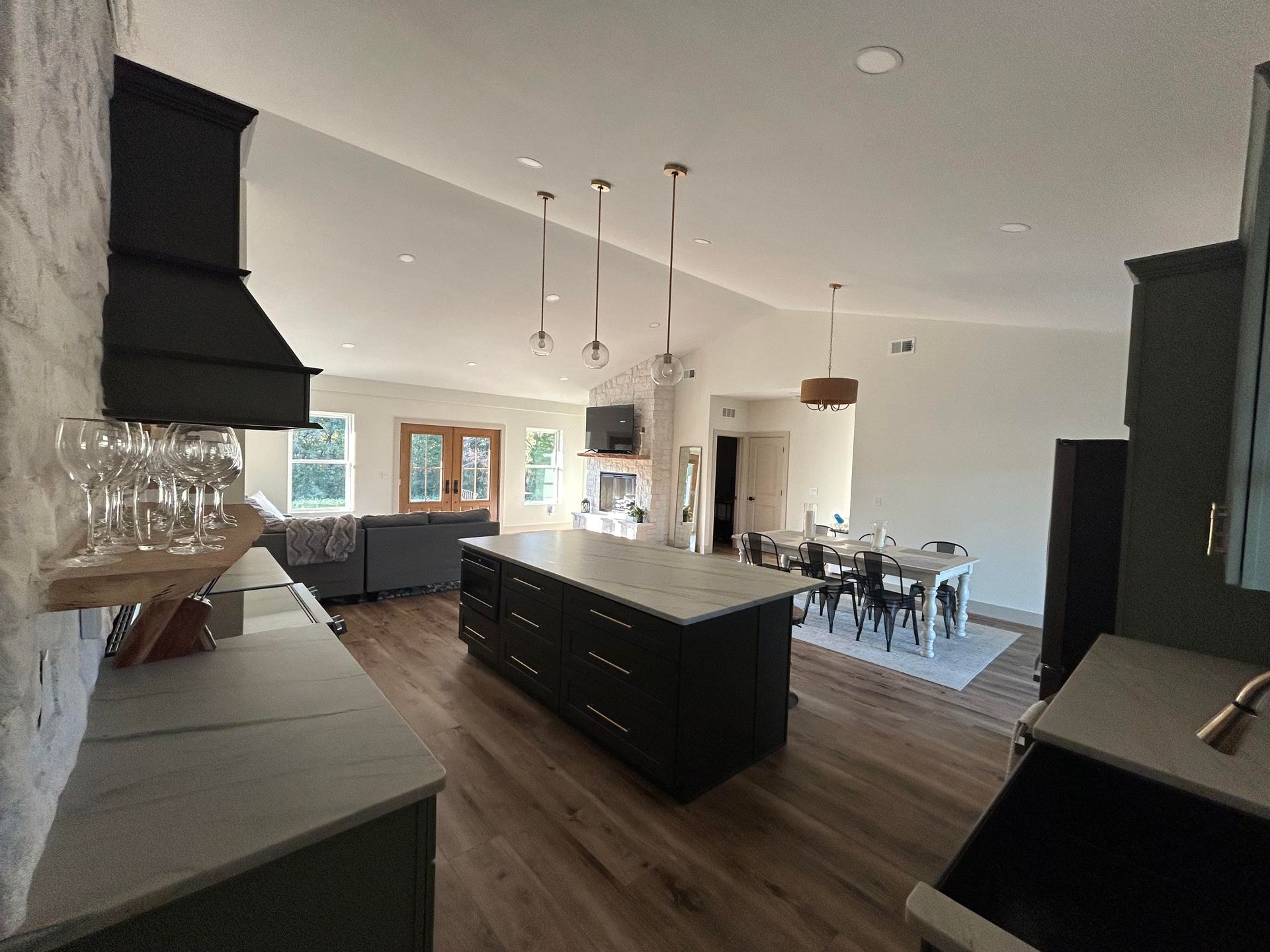 A spacious kitchen with a large island and dark cabinetry. Wooden floors, pendant lights, and a dining area are visible.