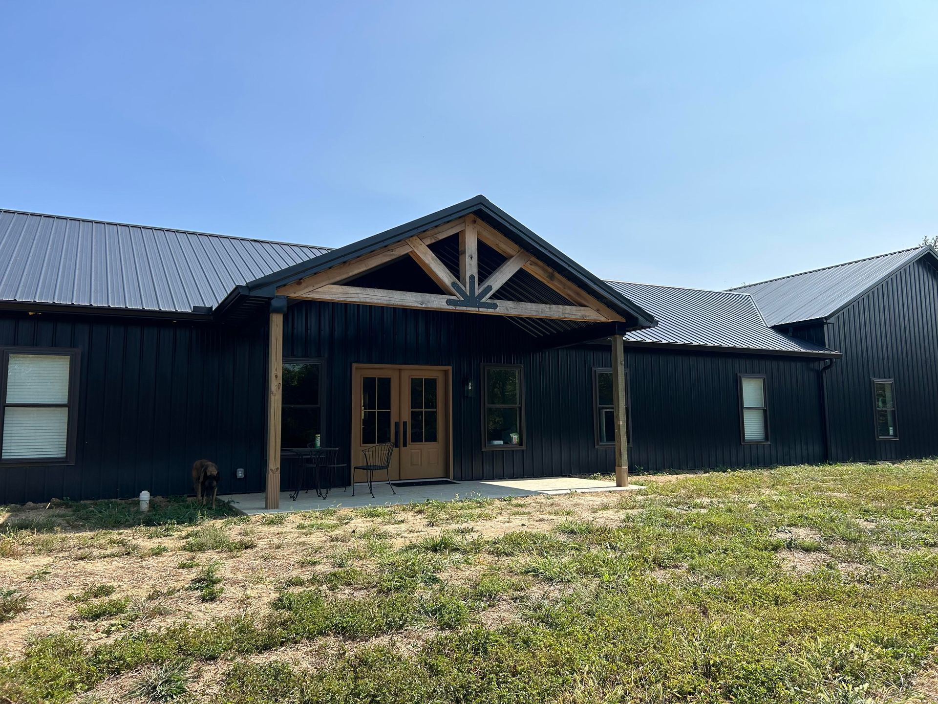 Black-sided modern building with a wooden porch and door, under a blue sky. The building is in a field.