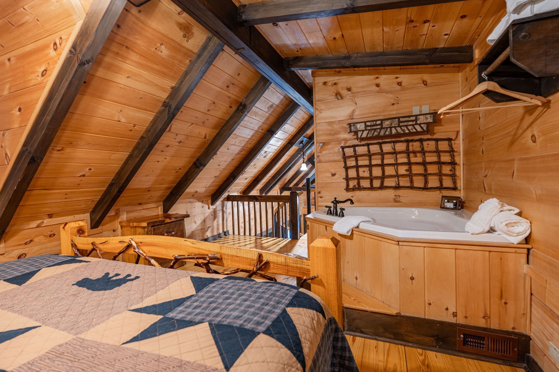 Wooden cabin loft with bed, jacuzzi, and exposed beams.
