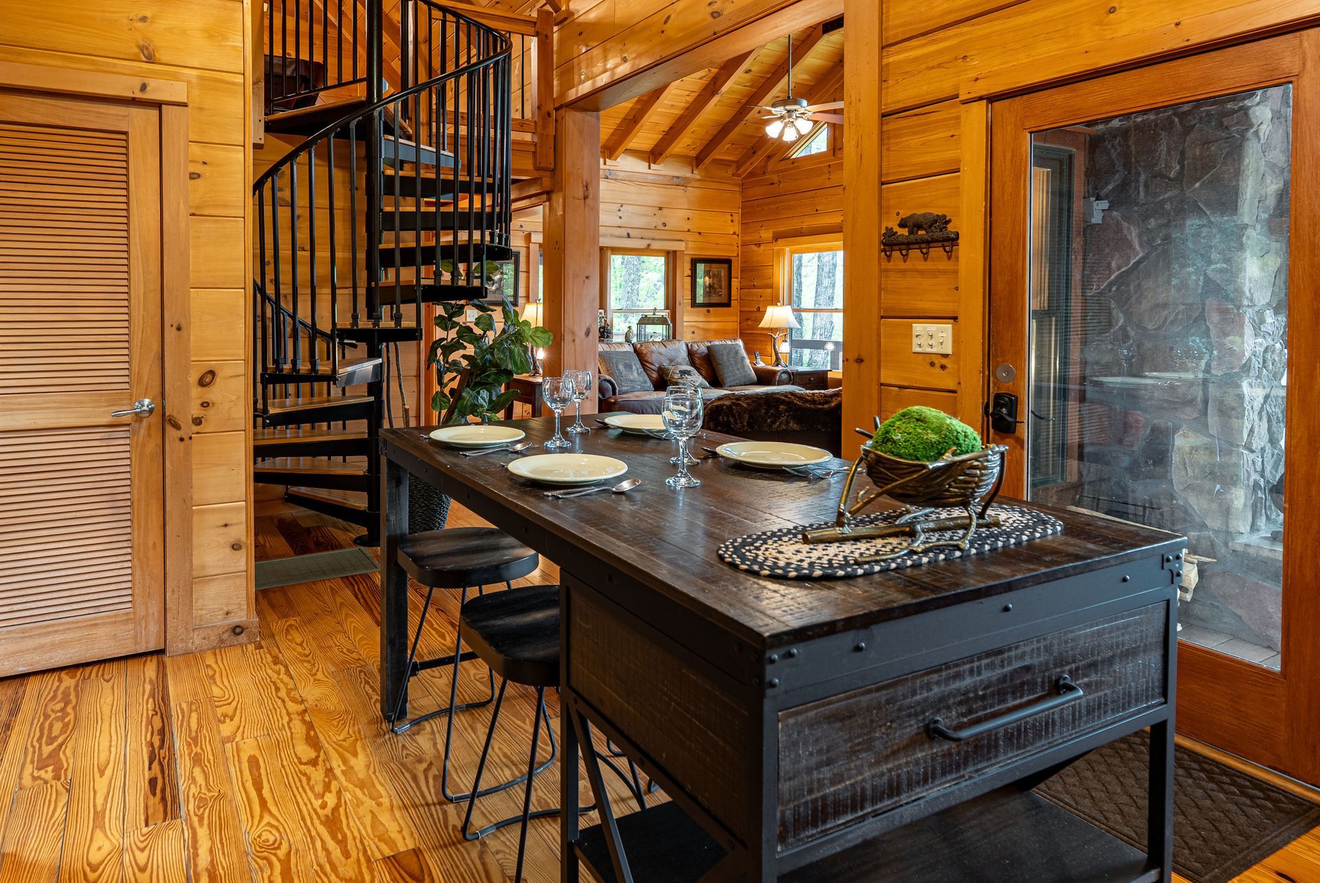Rustic cabin interior with dining table, spiral staircase, and open living area.
