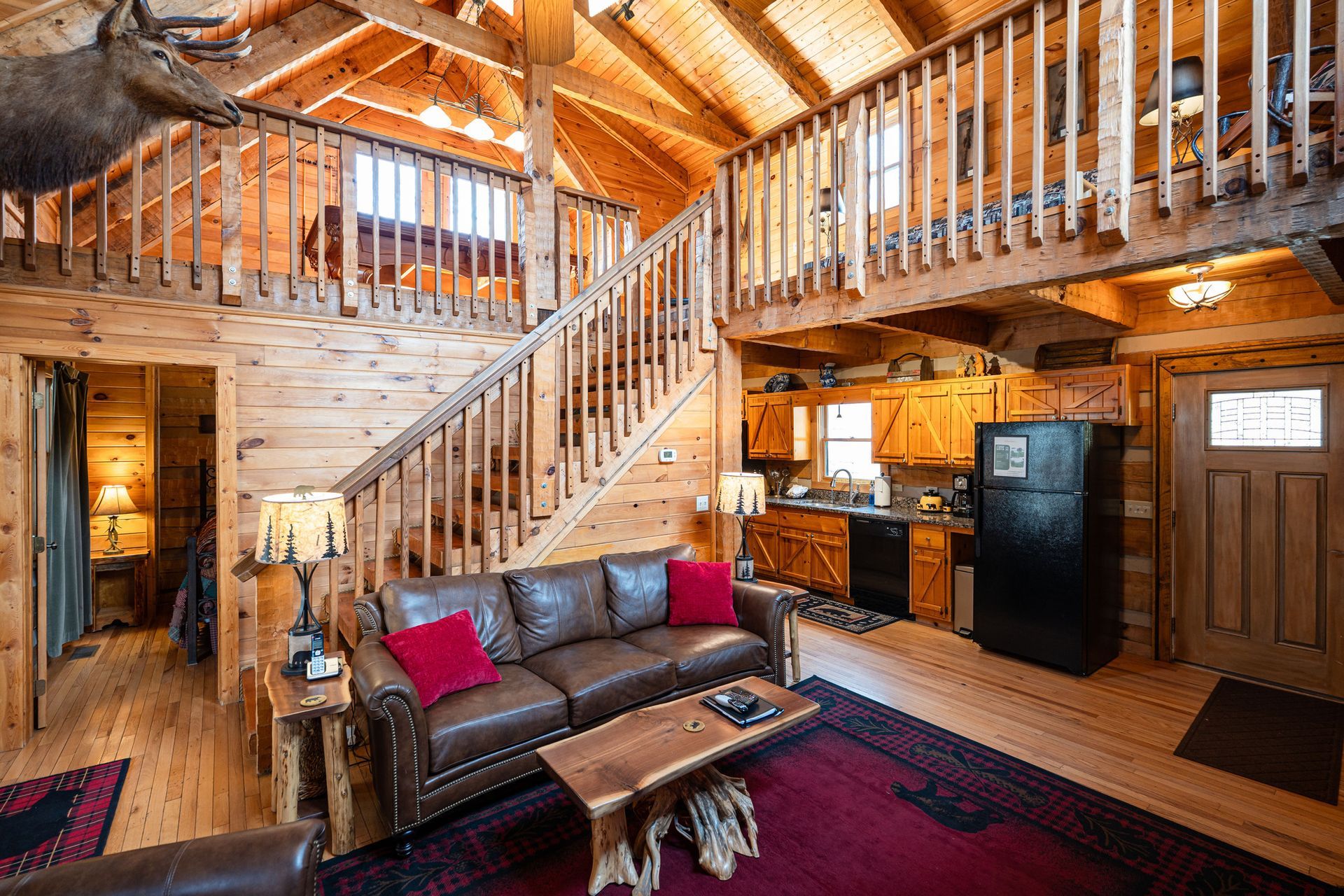 Cozy log cabin interior with loft, staircase, leather sofa, kitchen, and wood floors.