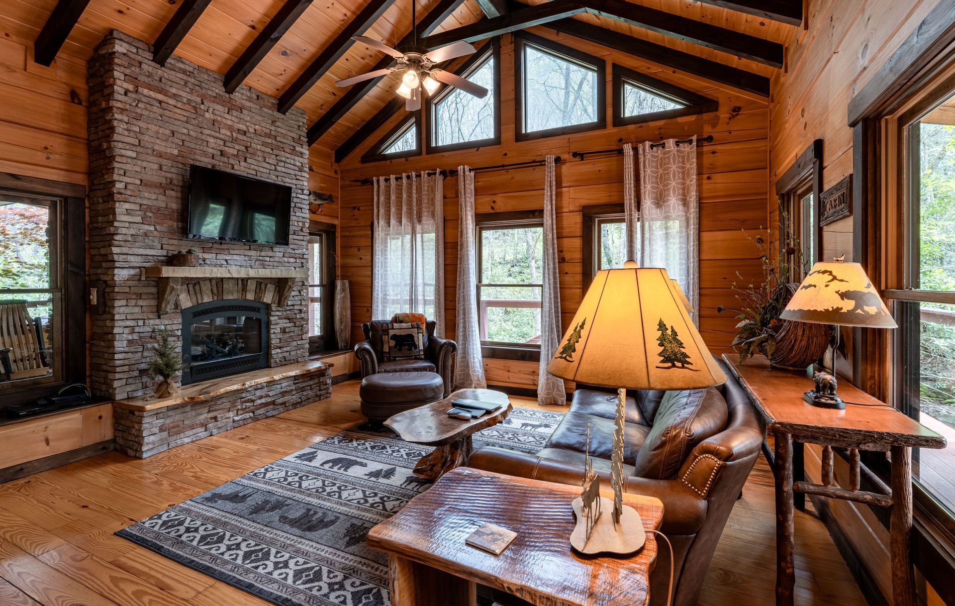 Cozy cabin living room with stone fireplace, wooden walls, leather furniture, and a rug.