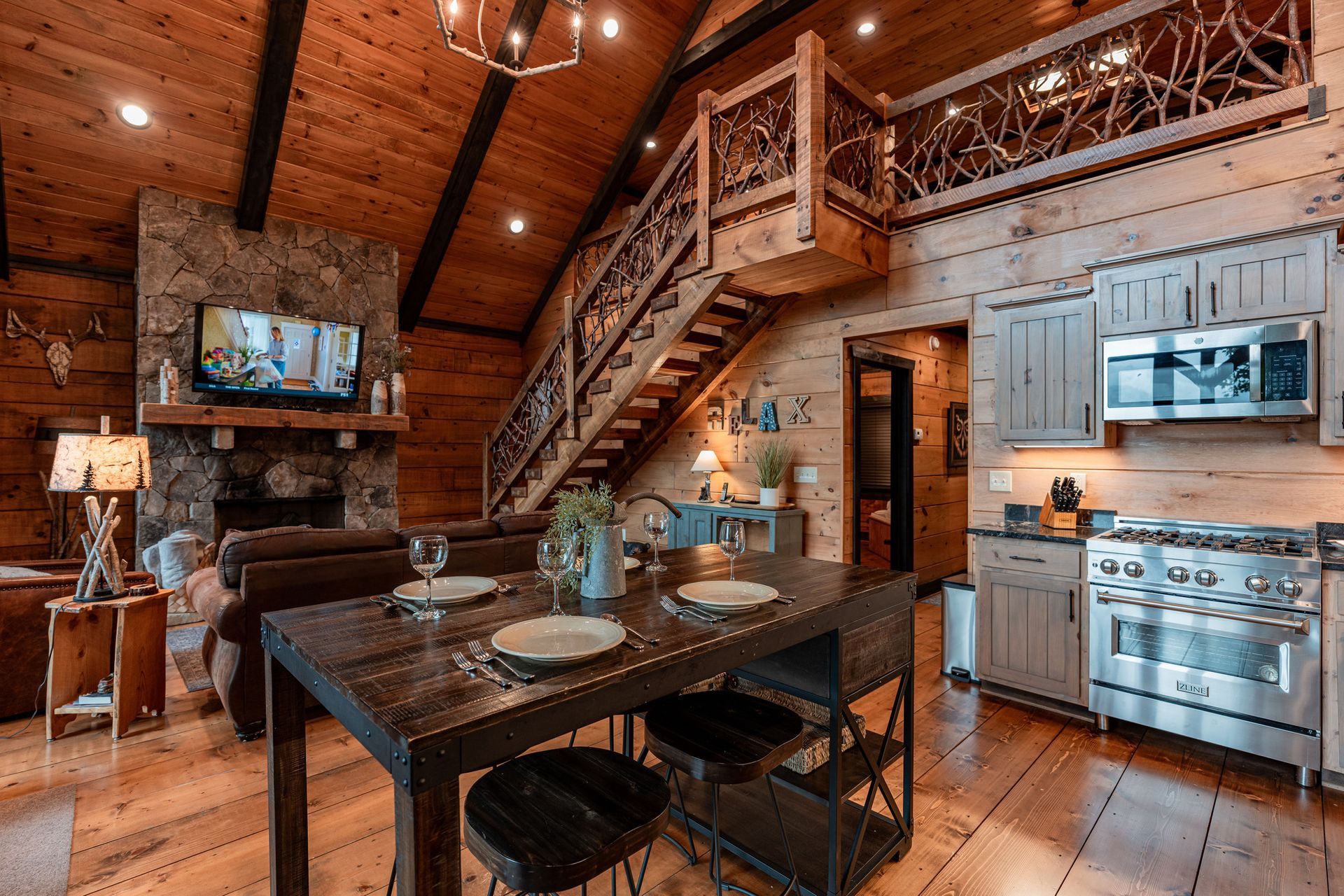 Rustic cabin interior with dining area, kitchen, stone fireplace, and loft.