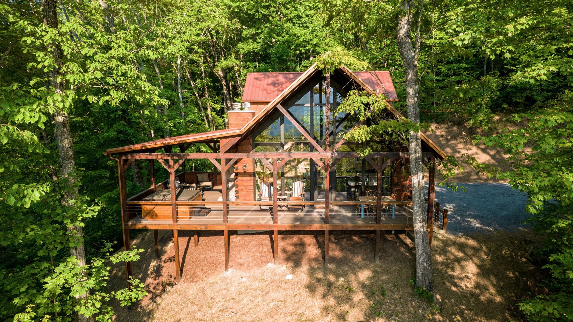 A-frame cabin nestled in trees with a large deck and red roof.