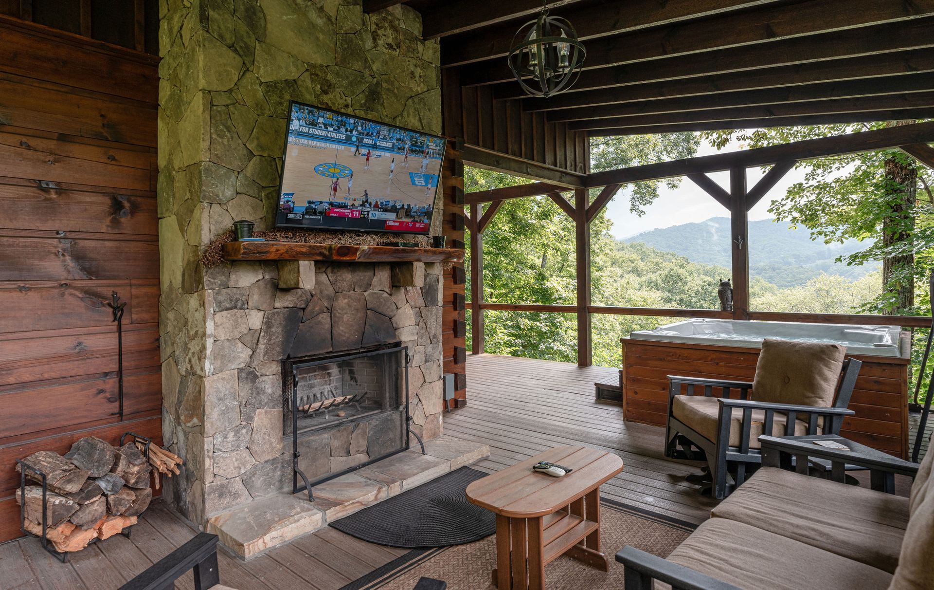 Outdoor covered porch with stone fireplace, TV, hot tub, and mountain view.
