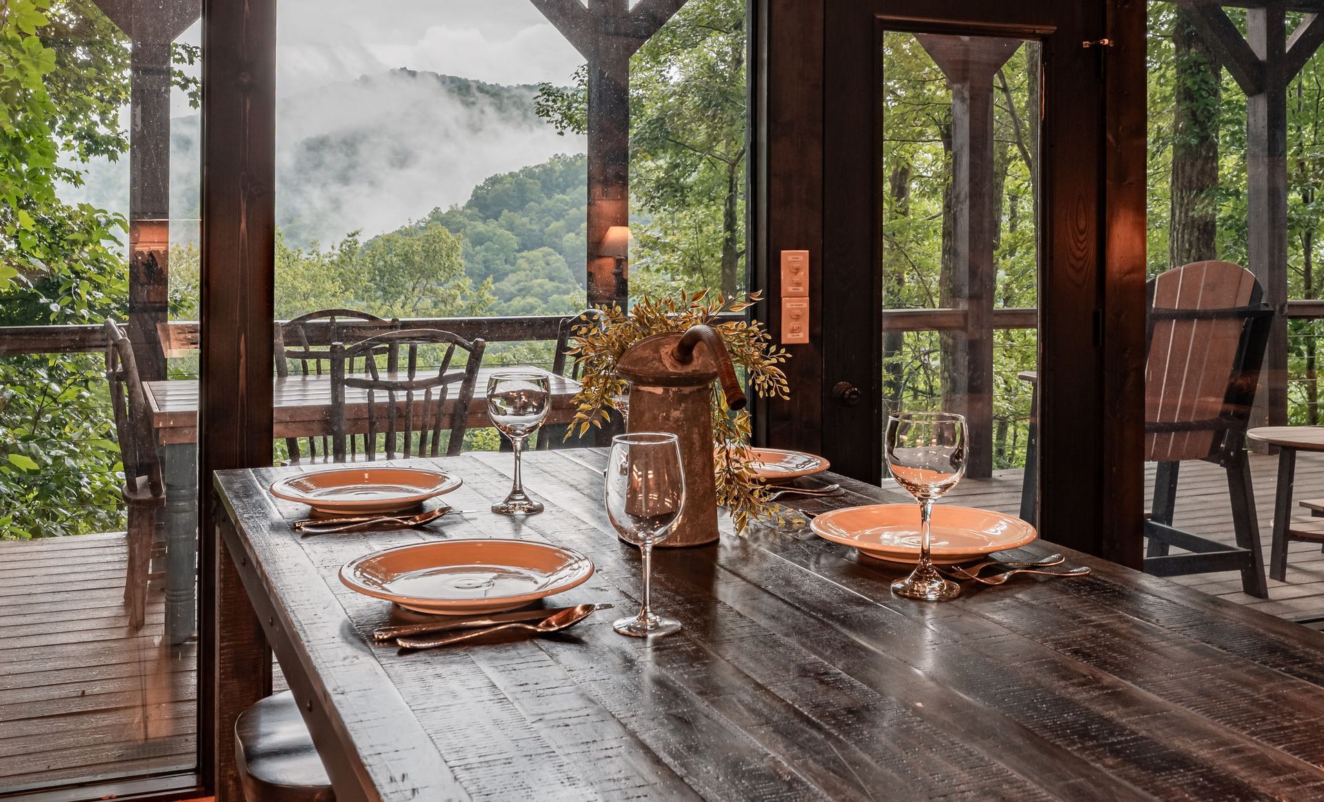 Wooden dining table set for a meal on a porch overlooking a misty mountain view.