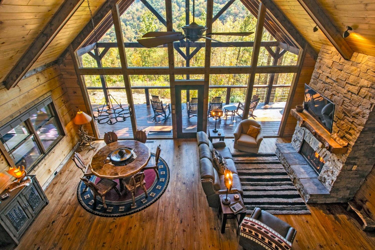 Spacious cabin interior with a large window, fireplace, and open floor plan, overlooking a deck.