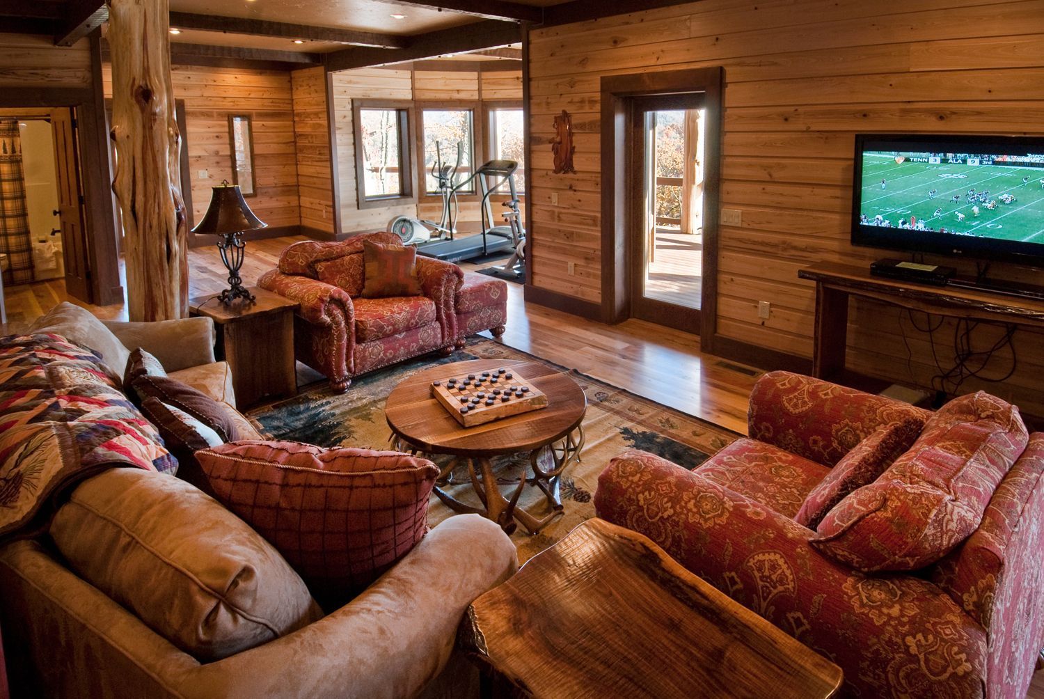 Cozy living room with wood paneled walls, a sofa, two armchairs, a coffee table, and a TV.