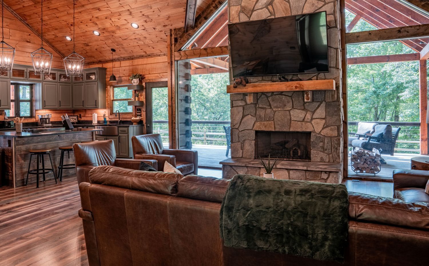 Cozy cabin interior with a fireplace, open kitchen, and outdoor deck. Brown wood and stone accents.