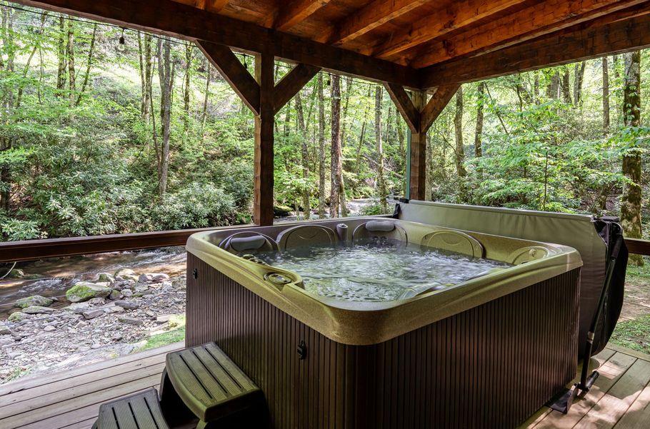 Cabin with porch and string lights next to a flowing river, surrounded by trees.
