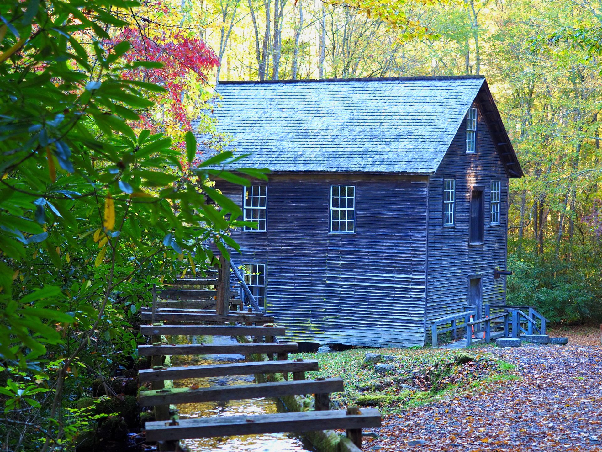 Historic wooden mill building, steps over creek, surrounded by autumn foliage.