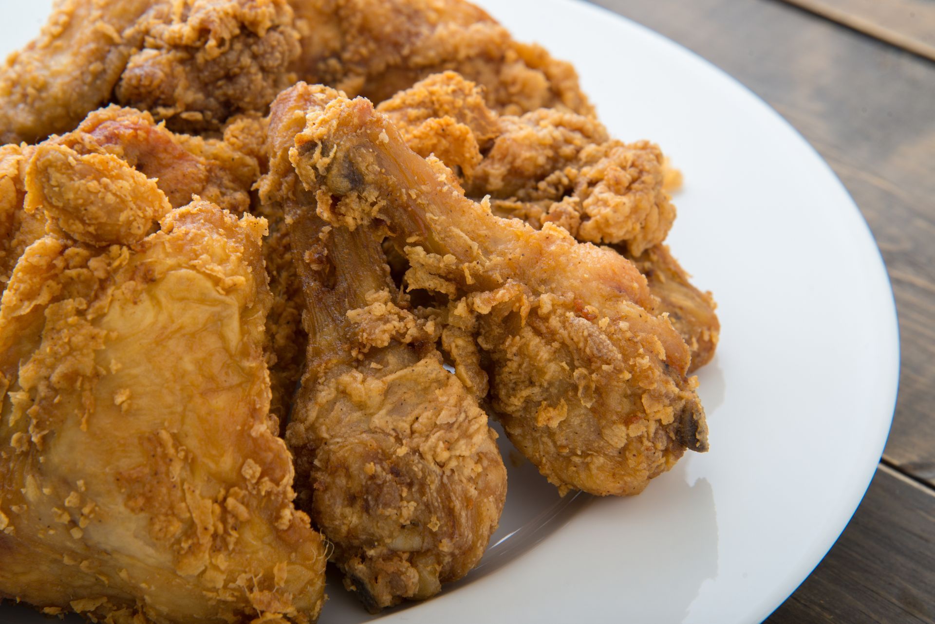 Fried chicken pieces on a white plate, set on a wooden surface.