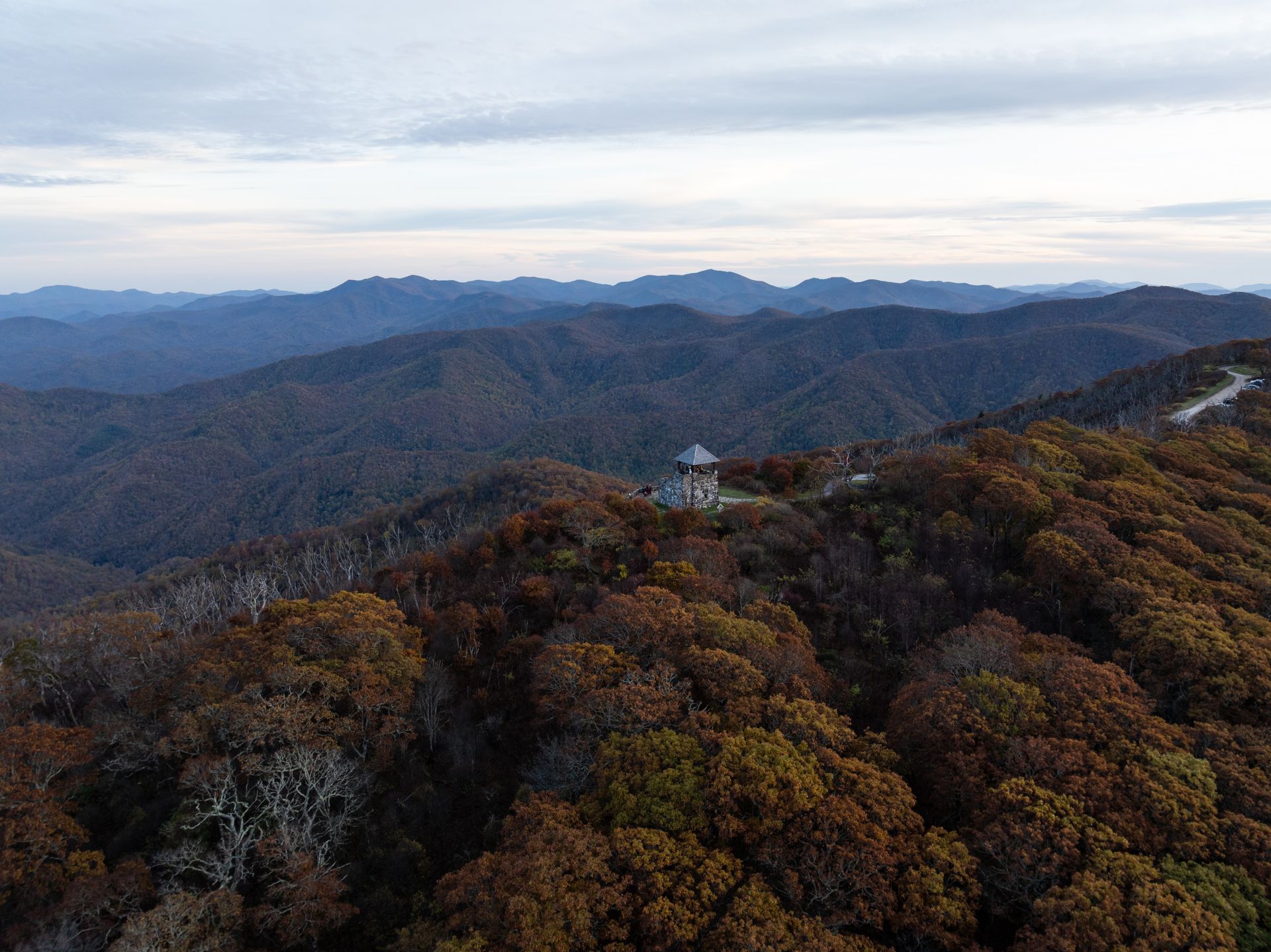 Aerial view of a mountain landscape with a small tower atop a ridge surrounded by fall foliage.