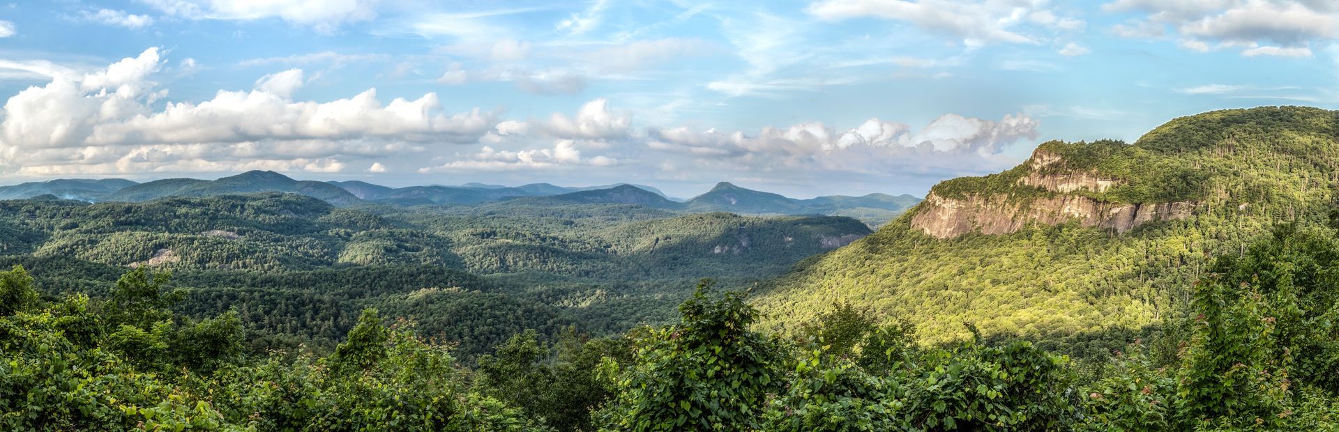 Panoramic view of a lush green mountain range under a partly cloudy sky.