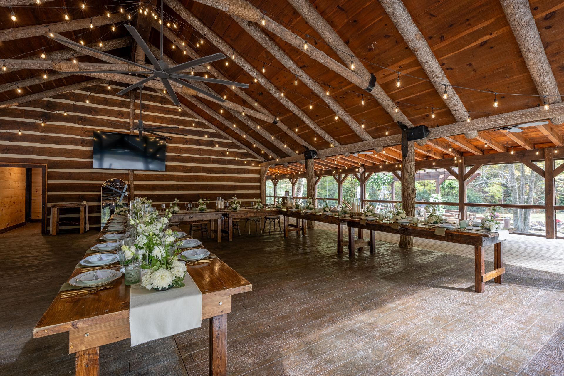 Event space with long tables set for dining under a wooden roof, strung with lights.