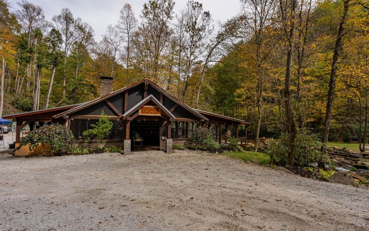Covered porch with fireplace, barrel bar, string lights, and dining tables, wood and stone elements.