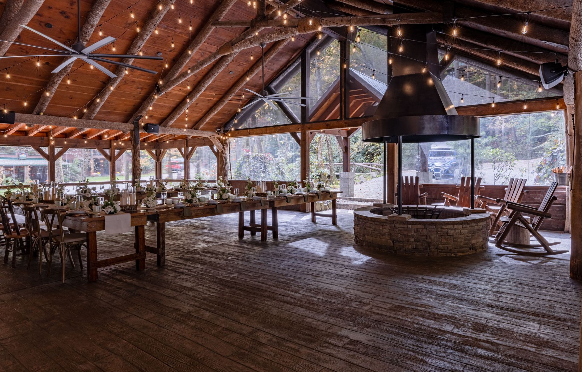 Rustic event space with long table set for dining, fireplace, and string lights.