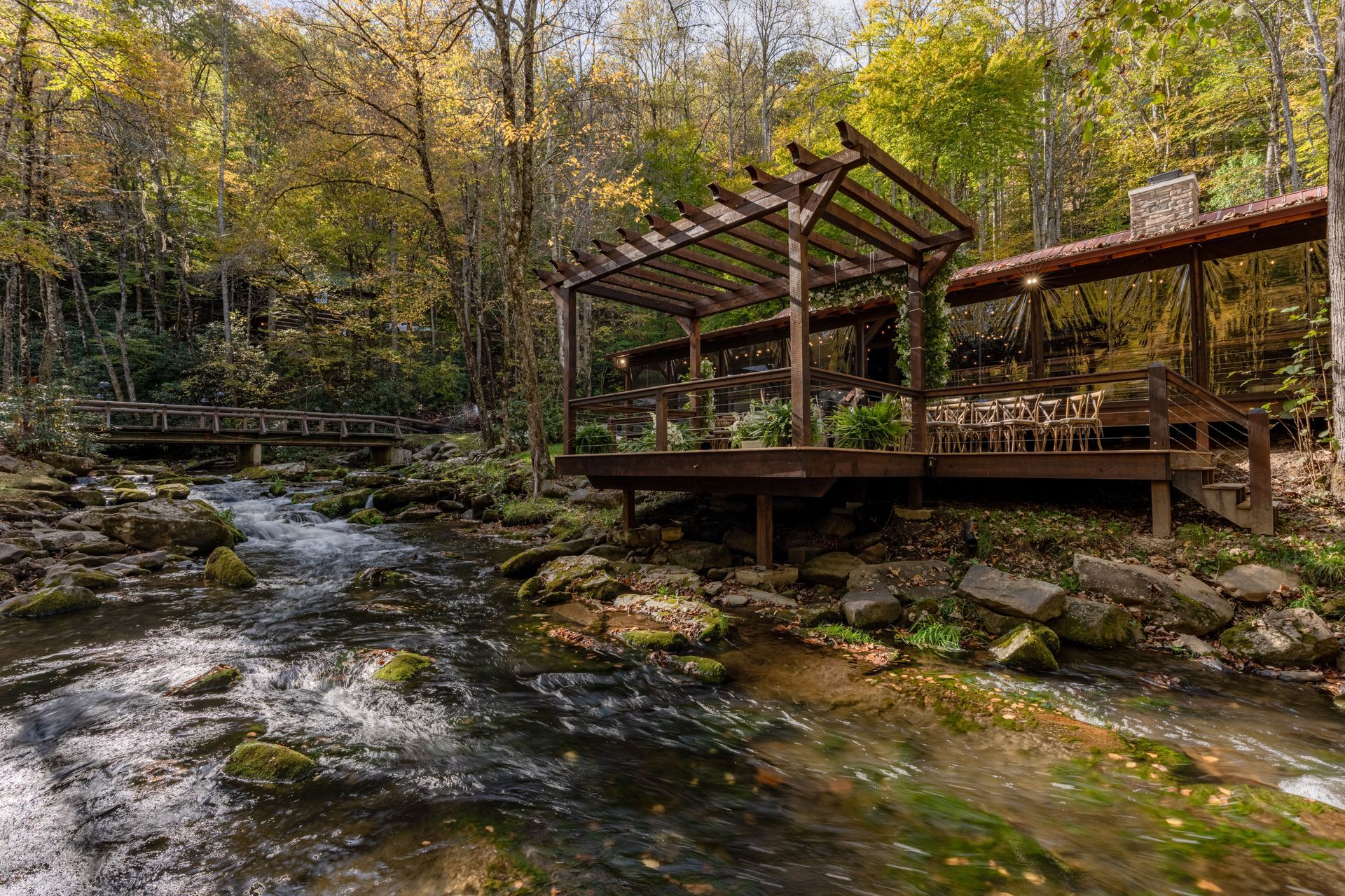 Wooden deck with pergola overlooking a flowing stream in a forest. Autumn foliage.