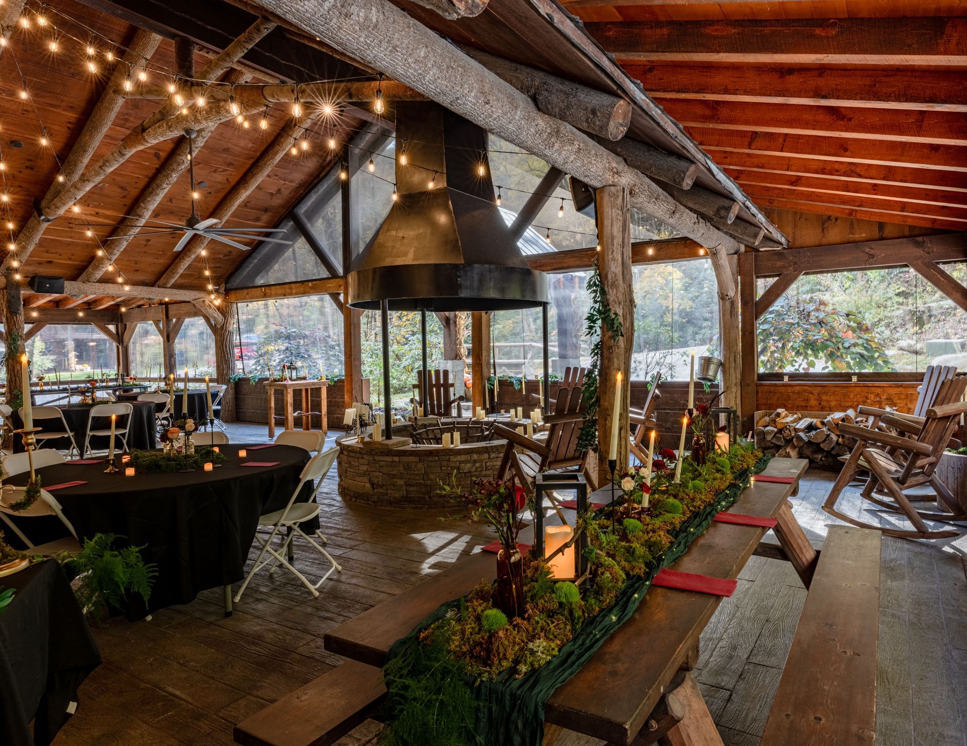 Covered outdoor event space with fireplace, tables, chairs, string lights, and greenery.
