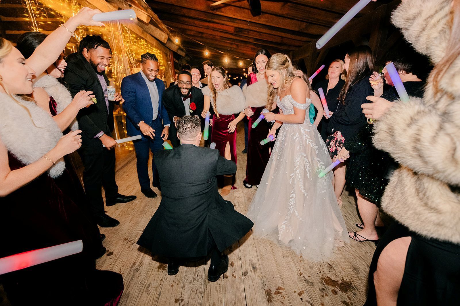 Wedding guests dance with glow sticks at a reception in a rustic hall.