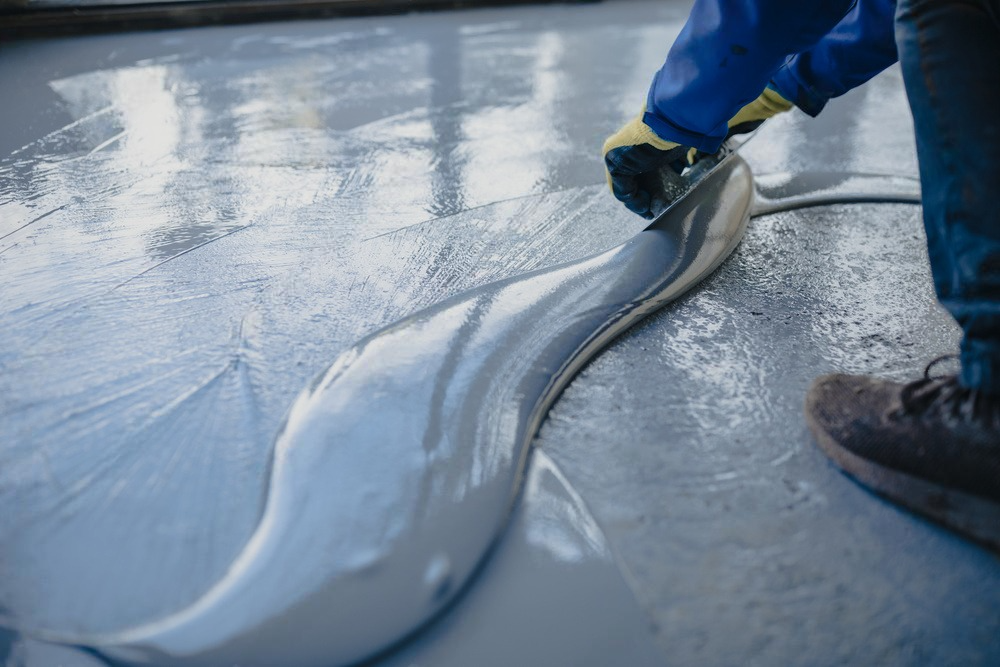 A person is spreading concrete on a concrete floor.